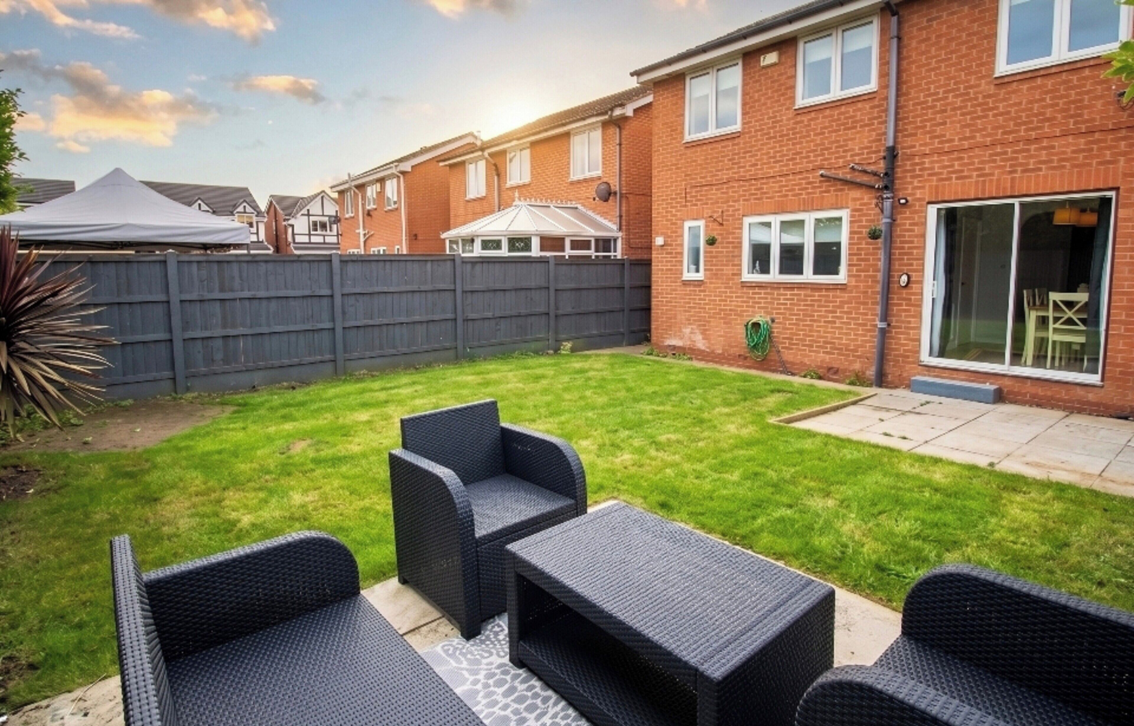 A backyard with a patio set, a brick house, and a fenced area.