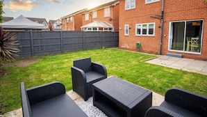 A backyard with a patio set, a brick house, and a fenced area.