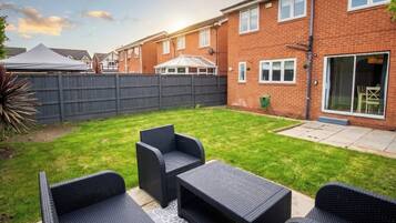 A backyard with a patio set, a brick house, and a fenced area.
