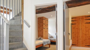 A bedroom with a bed, a wooden wardrobe, and a staircase. - Mill House (Lostwithiel)