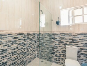 Un baño moderno con cabina de ducha de vidrio, inodoro y salpicadero de azulejos con diseño.
