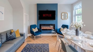 Una sala de estar moderna con chimenea, un comedor y un televisor grande montado en la pared.