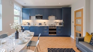 Una cocina moderna con armarios azules, electrodomésticos de acero inoxidable y un comedor con mesa dispuesta para cuatro.