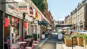 Una calle estrecha con un restaurante de sushi a la izquierda y una cafetería a la derecha.