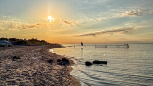 A beach with a pier extending into calm waters, a clear sky, and a sunset. - Stunning home in Otterup with WiFi (Otterup)