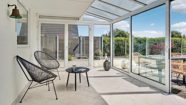 A conservatory with a glass roof, two wicker chairs, a small table, and a bell on the wall. - Stunning home in Otterup with WiFi (Otterup)