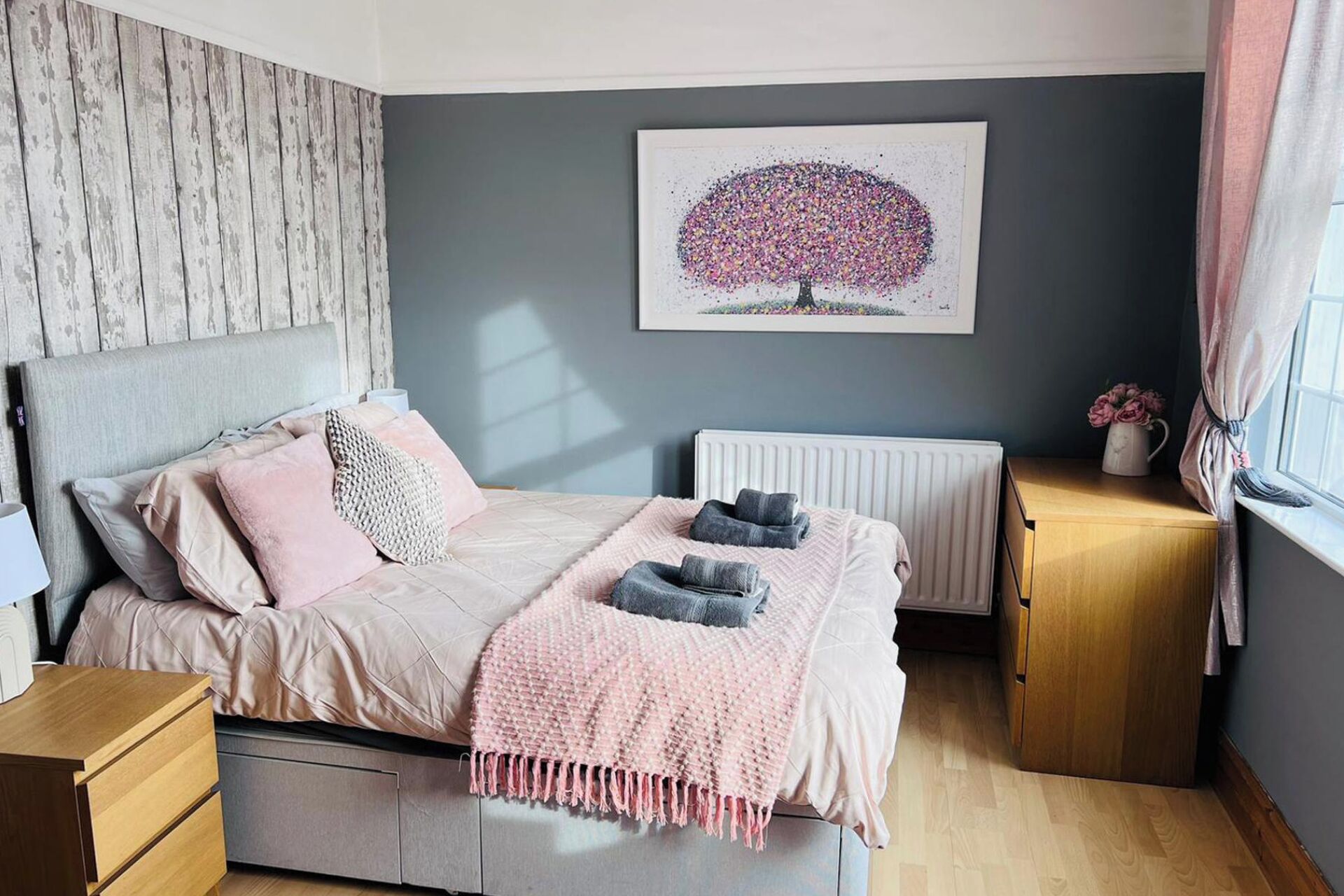 A bedroom with a bed, bedside tables, a radiator, and a window with curtains.