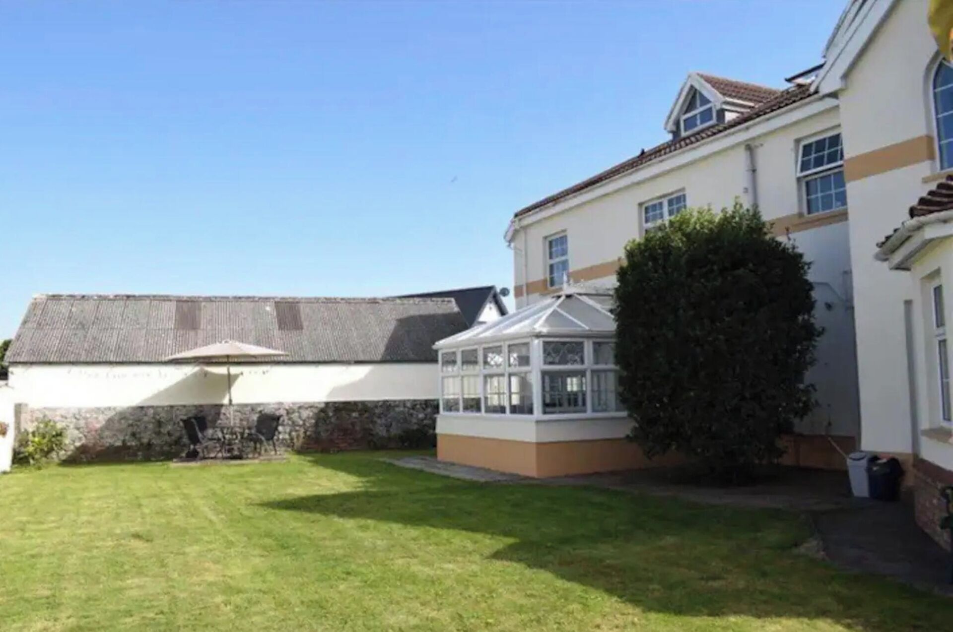A house with a conservatory, a lawn, and a stone wall.