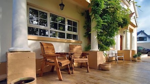 Um deck de madeira com duas cadeiras, uma mesa, um vaso de planta e uma janela com vista para árvores.