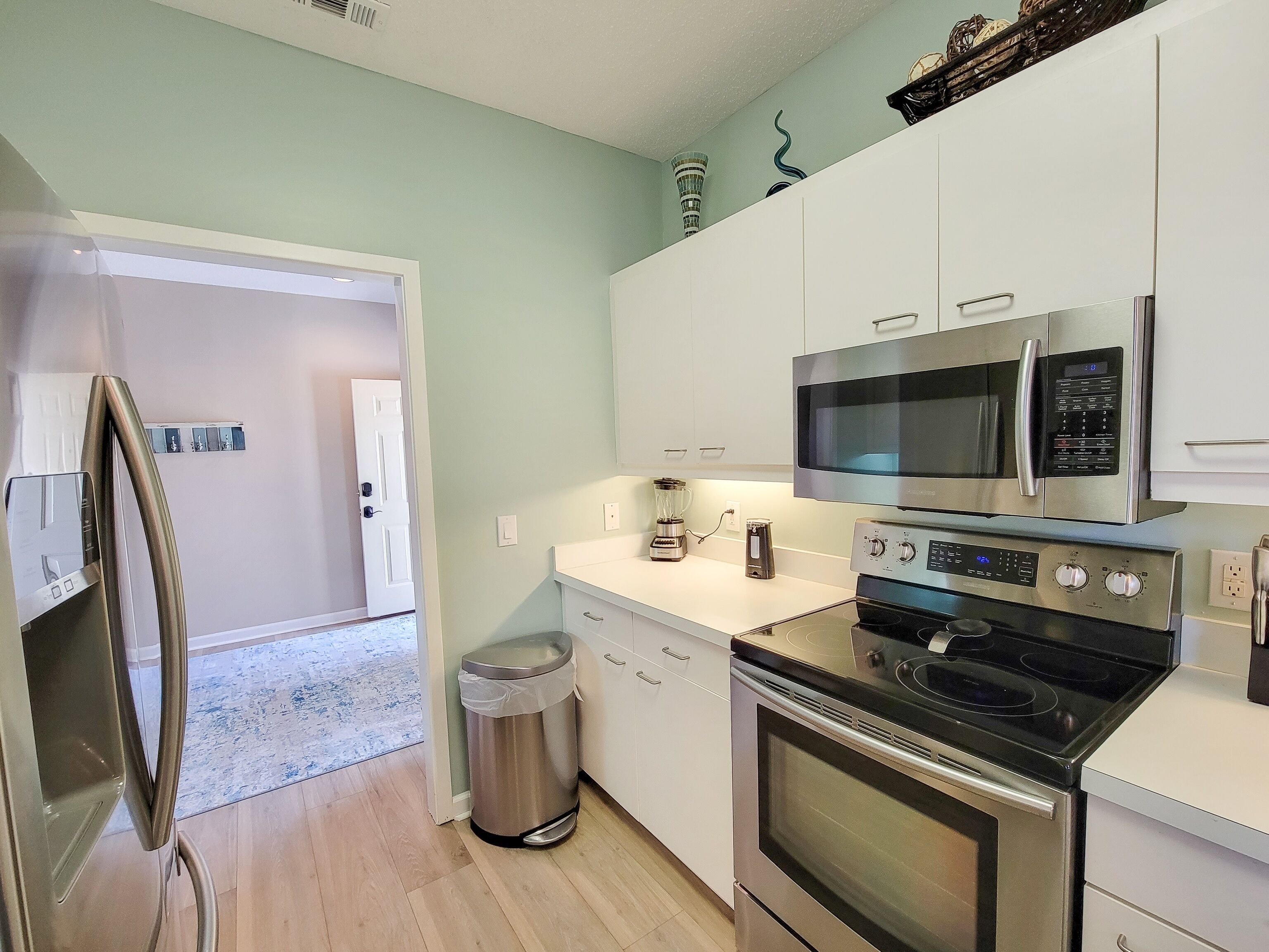 A modern kitchen with stainless steel appliances, including a refrigerator, microwave, and oven. There is a trash can and a coffee maker on the counter.