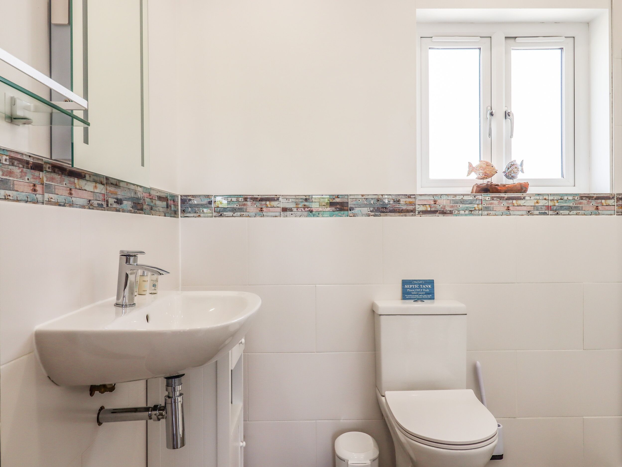 A bathroom with a white sink, toilet, and a window above the toilet.