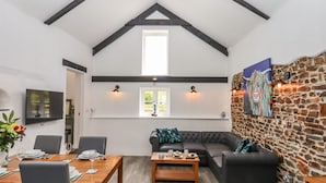 A dining area with a wooden table and chairs, a sofa, and a stone wall with a painting. - Strawberry Bank - Kingfisher (Holsworthy)