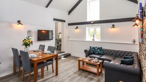 A modern living room with a dining area, a sofa, and a TV mounted on the wall. - Strawberry Bank - Kingfisher (Holsworthy)