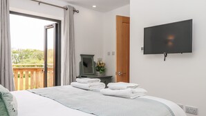 A bedroom with a bed, a television, a wooden door, and a view of greenery outside. - Strawberry Bank - Kingfisher (Holsworthy)