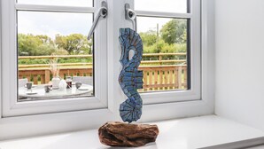 A window with a wooden sculpture on the sill and a view of an outdoor deck with a wooden railing and greenery. - Strawberry Bank - Kingfisher (Holsworthy)