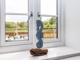 A window with a wooden sculpture on the sill and a view of an outdoor deck with a wooden railing and greenery.