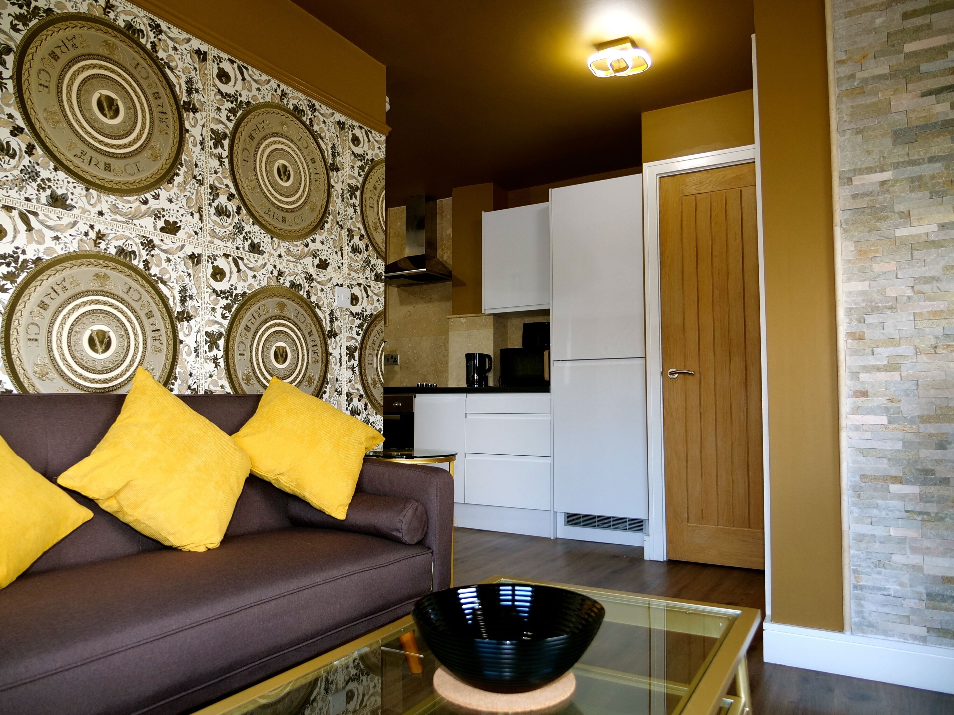 Una sala de estar moderna con un sofá marrón, cojines amarillos y una mesa de centro de vidrio.