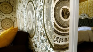 Une pièce avec un papier peint à motifs, un lit avec une tête de lit sombre et un oreiller jaune sur le côté gauche.