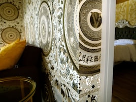 A room with a patterned wallpaper, a bed with a dark headboard, and a yellow pillow on the left.