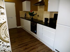 A compact kitchen with white cabinetry, a black countertop, and a wooden floor.