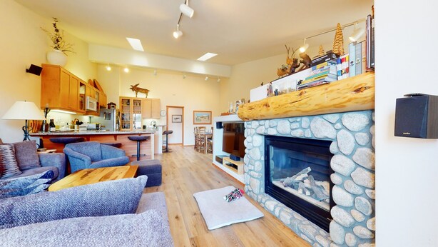 A modern living room with a stone fireplace, a kitchen in the background, and a dining area.