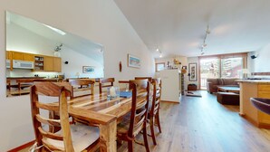 A spacious living area with a wooden dining table and chairs, a kitchen with wooden cabinets, and a large window providing natural light.