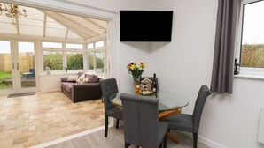 A modern living room with a glass dining table, grey chairs, a sofa, and a flat-screen TV mounted on the wall. - Ty Cariad (Carmarthen)
