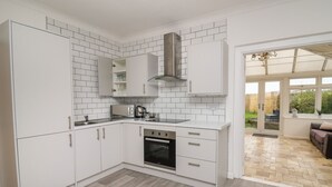 A modern kitchen with white cabinetry, a built-in oven, and a microwave. There is a window providing natural light and a view of the outdoors. - Ty Cariad (Carmarthen)