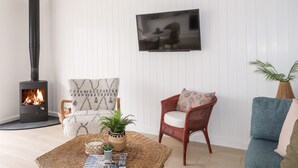 Ett mysigt vardagsrum med en öppen spis, en bekväm fåtölj, en tv och ett litet bord med tidningar och en växt.