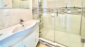 Ein modernes Badezimmer mit einer gläsernen Duschkabine, einem weißen Waschbecken und einem großen Spiegel.