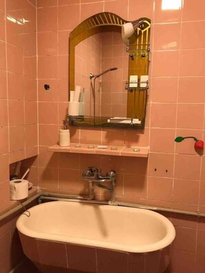 A bathroom with a freestanding bathtub, a mirror with a wooden frame, and a shelf with toiletries. - Impeccable 2-bed Apartment in Central Tbilisi (Tbilisi)