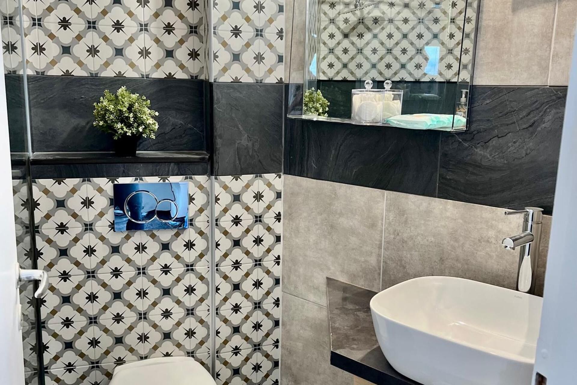 A bathroom with patterned tiles, a white sink, and a mirror.