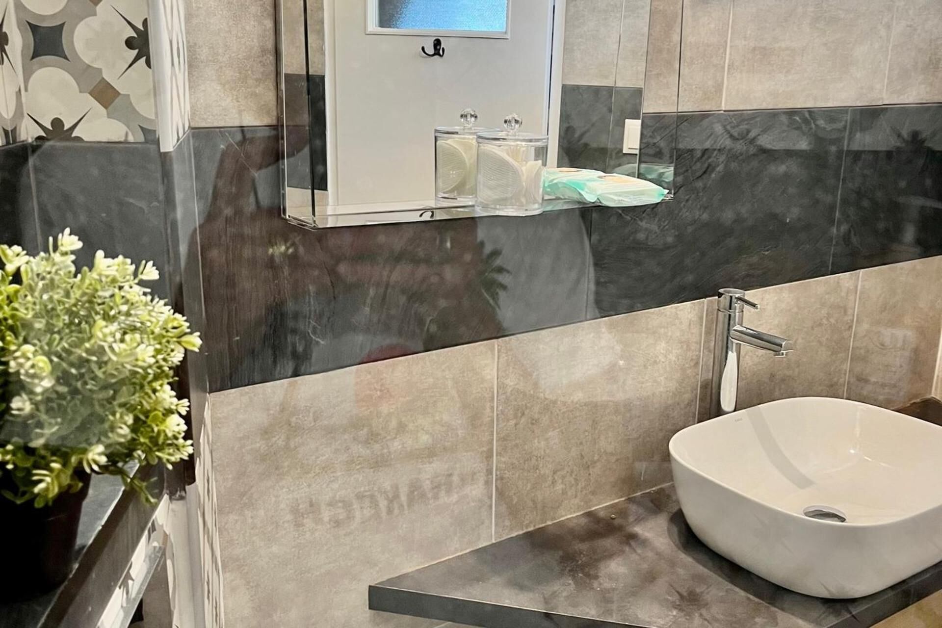 Un bagno moderno con un lavandino bianco, uno specchio e uno scaffale con articoli da toilette.