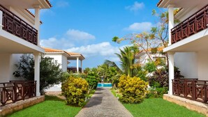 A pathway leading to a pool surrounded by lush greenery and white buildings with brown railings.