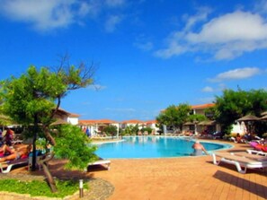 A pool area with lounge chairs and umbrellas, surrounded by buildings with red roofs.