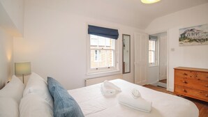 Una camera da letto con un letto, una cassettiera, una finestra vista edifici e un quadro appeso al muro.