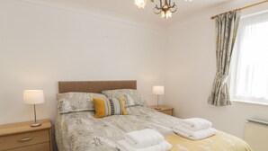 Una cama bien hecha con ropa de cama floral, dos lámparas de noche y una ventana con cortinas.