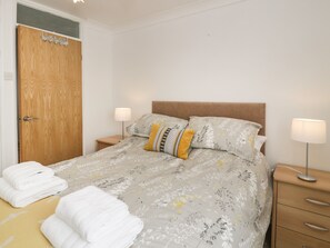 Ein ordentlich bezogenes Bett mit Blumenmuster, zwei Nachttischlampen und ein Nachttisch mit einer Lampe.