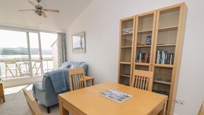 Una habitación con una mesa de madera, sillas azules, una estantería y vistas al exterior.