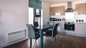 A modern kitchen with a dining area, featuring a table and chairs, a microwave, oven, and cabinets. - Birmingham Luxury Apartment - Free Wifi (Birmingham)