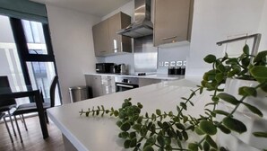 A modern kitchen with stainless steel appliances, a white countertop, and a view of the city through large windows. - Birmingham Luxury Apartment - Free Wifi (Birmingham)