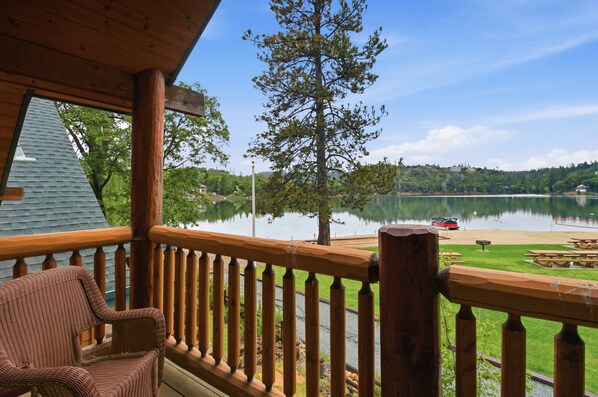 Une terrasse en bois avec une chaise, donnant sur un lac paisible, avec un quai et des tables de pique-nique.