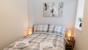 Ein ordentlich bezogenes Bett mit Karo-Bettwäsche, zwei Nachttischlampen und ein Bild an der Wand.