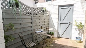 Eine Terrasse mit einem Holztisch und Stühlen, einer Weinflasche und Kübelpflanzen.