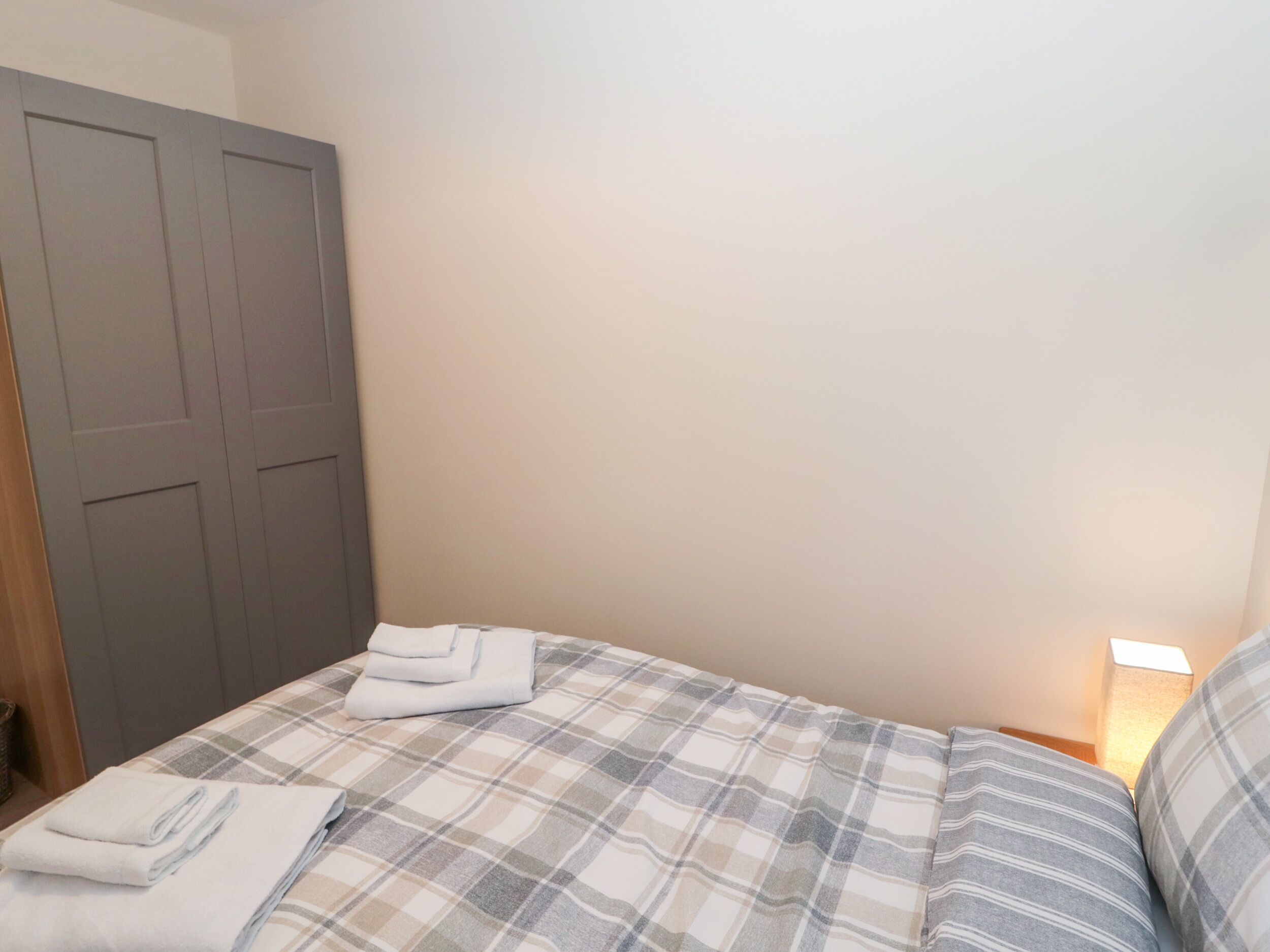 A bedroom with a bed, a grey wardrobe, and a bedside lamp.