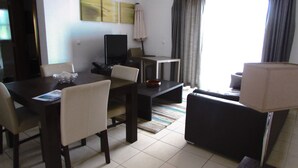 A hotel room with a dining table, chairs, a TV, a sofa, and a lamp. - Lovely 2-bed Apartment in Santa Maria (Sal)