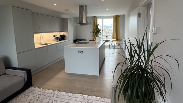 A modern kitchen with a central island, a dining area with chairs, and a large potted plant. - Immaculate 2-bed Apartment in London (London)