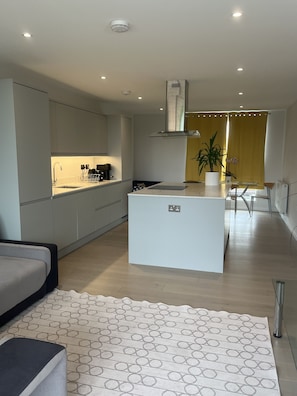 A modern kitchen with a central island, a dining area with yellow curtains, and a living space with a patterned rug. - Immaculate 2-bed Apartment in London (London)