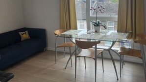 A modern living room with a glass dining table, a blue sofa, and a view of a cityscape through large windows. - Immaculate 2-bed Apartment in London (London)