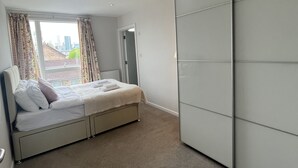 A bedroom with a bed, a wardrobe, and a window with curtains. - Immaculate 2-bed Apartment in London (London)